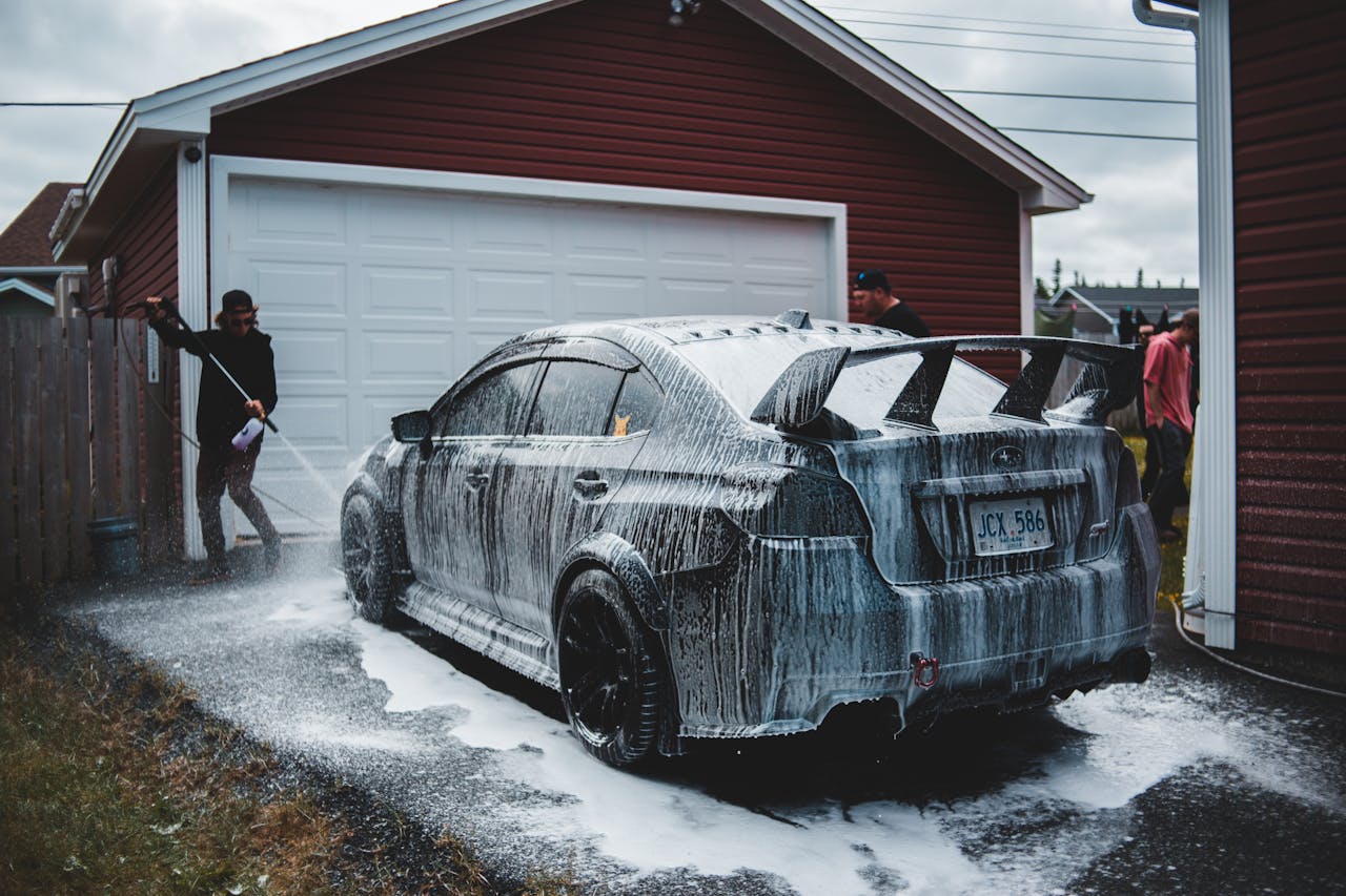 Full body of unrecognizable male in casual clothing washing front part of expensive tuned vehicle while standing in front of door to garage