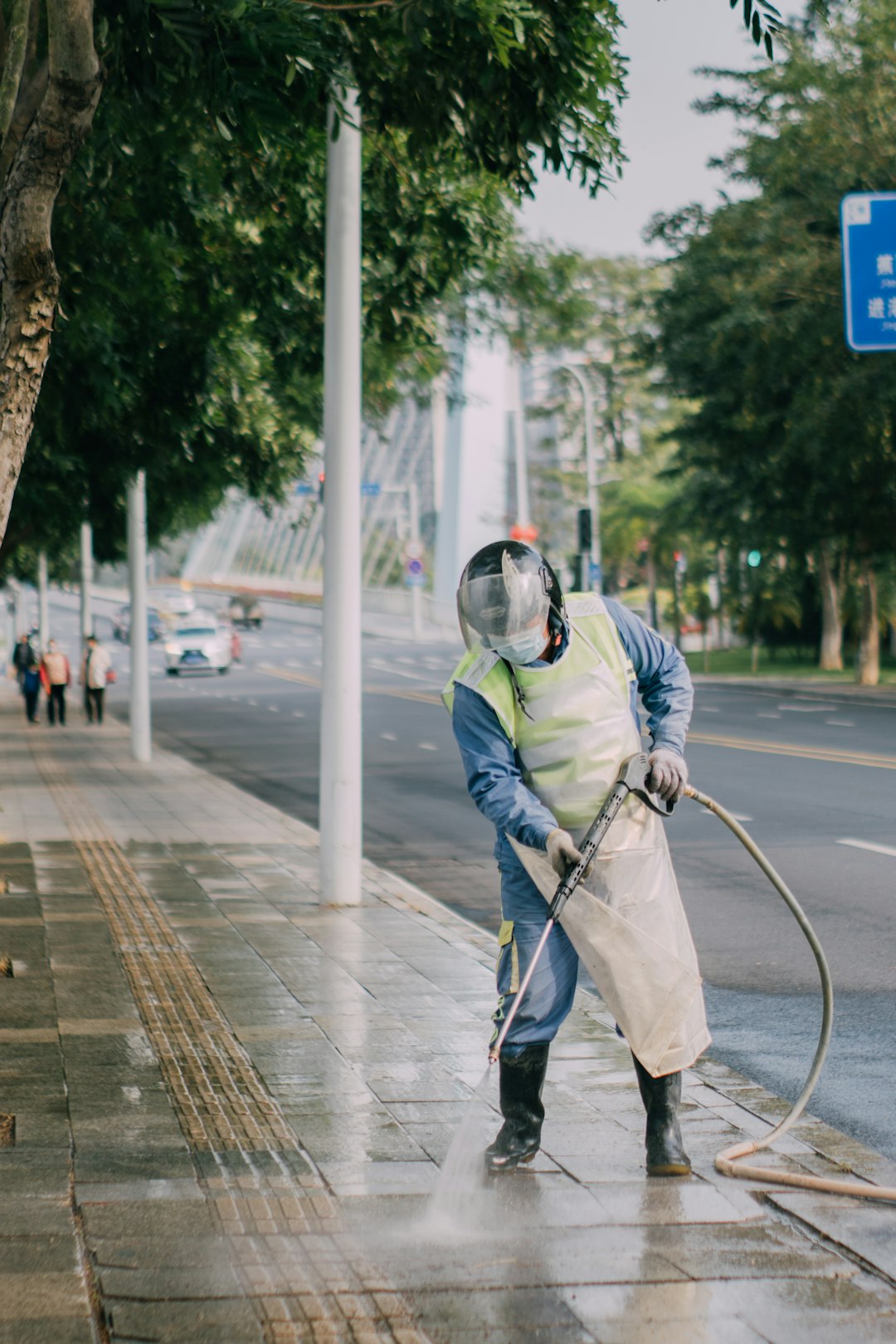 a-man-in-a-yellow-vest-is-spraying-water-on-a-sidewalk-0liyvdj6xuk